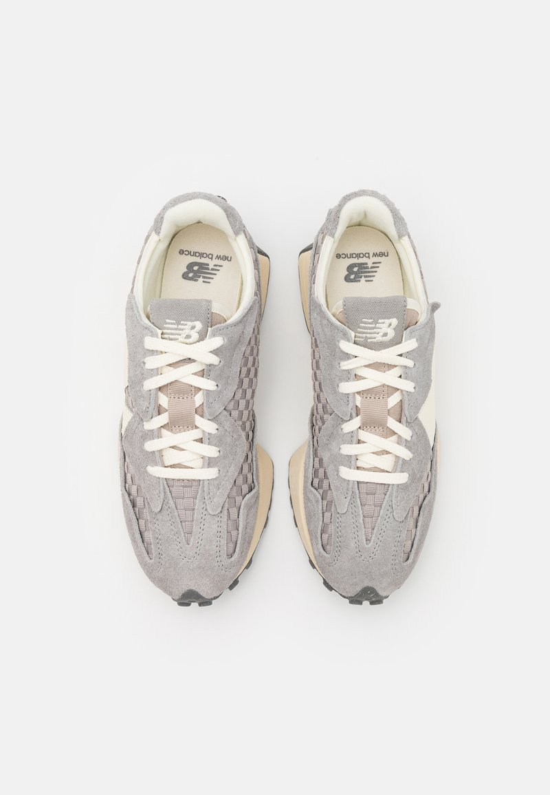 Zapatillas de ante gris con textura trenzada, cordones blancos, acentos beige y suela de goma negra, que cuentan con el logotipo de New Balance en la lengüeta.