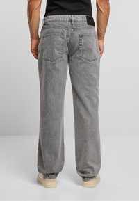 Pantaloni in denim grigio con vestibilità rilassata, dotati di quattro tasche, texture liscia e polsini elasticizzati alle caviglie. Dettaglio in pelle sulla vita.