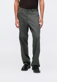 Szare, dopasowane spodnie o prostym kroju, z przednią kieszenią, paskami na pasek i zapięciem na guzik. Noszone z czarnymi butami.