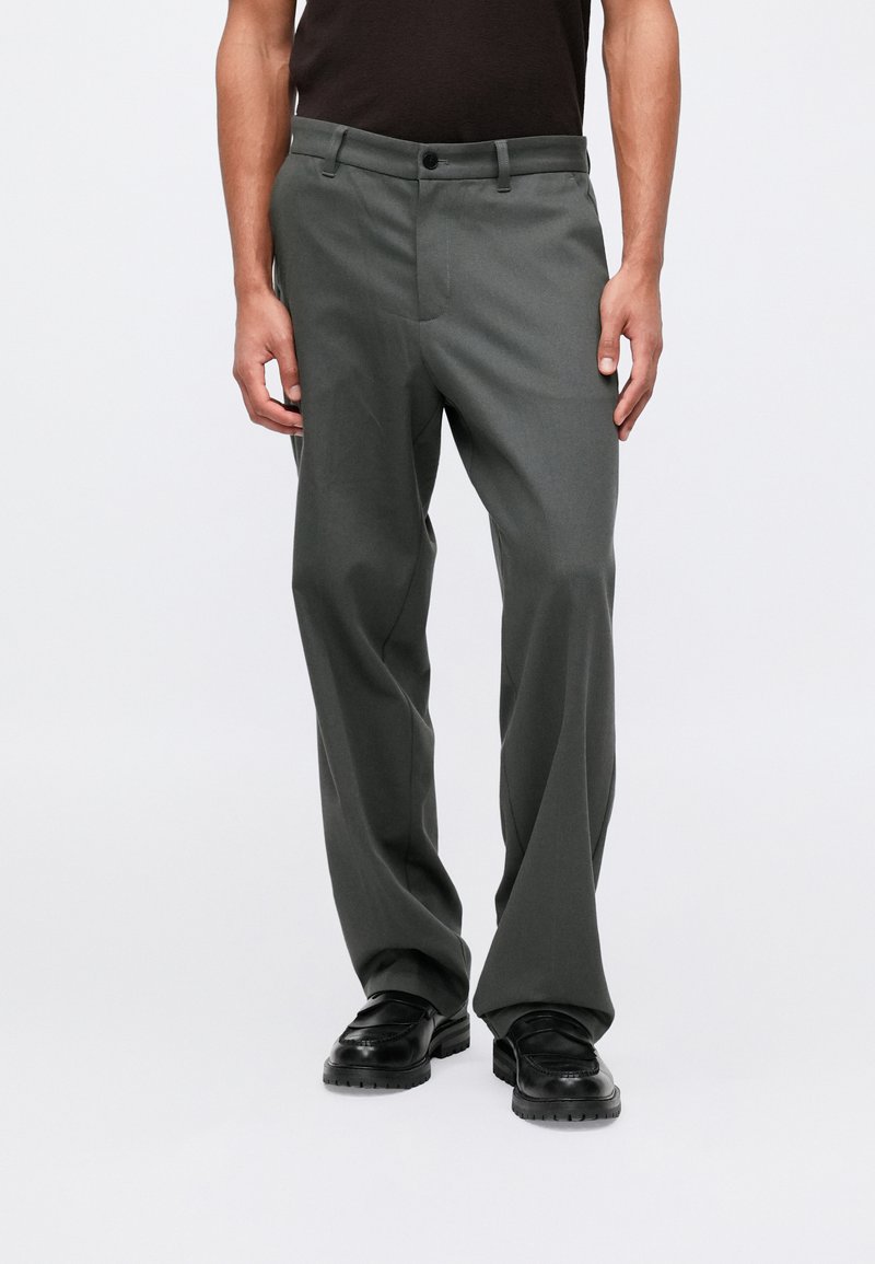 Szare, dopasowane spodnie o prostym kroju, z przednią kieszenią, paskami na pasek i zapięciem na guzik. Noszone z czarnymi butami.