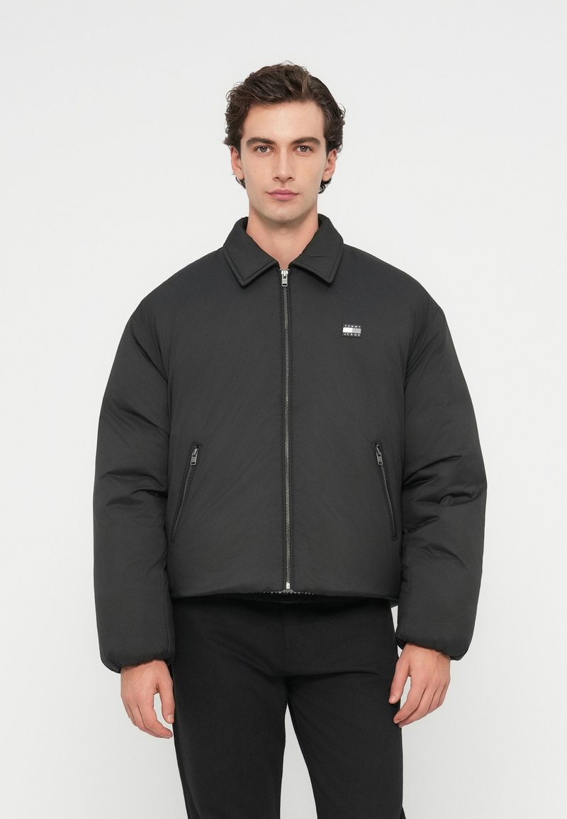 Mustapaitainen toppatakki, jossa on kaulus, etuvetoketju, sivuvetoketjulliset taskut ja logoyksityiskohta rintaketjussa. Sileä pinta, lyhennetty malli.