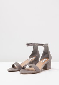 Gray suede heeled sandals with ankle strap, open toe, and block heel. Smooth texture and minimal design. Adaptable for various outfits.