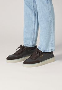 Dark brown sneakers made of leather and suede with a white rubber sole. Features include round laces and logo detailing on the side.