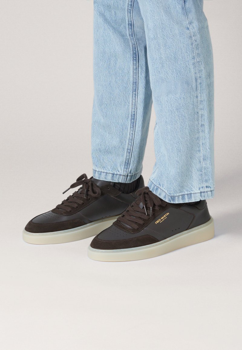 Dark brown sneakers made of leather and suede with a white rubber sole. Features include round laces and logo detailing on the side.