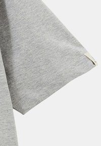 T-shirt en coton gris montrant un gros plan de la manche avec une texture lisse, un ourlet cousu et une petite étiquette attachée.