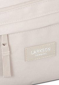 Borsa in tessuto beige chiaro con superficie testurizzata, dotata di una tasca con zip e di un'etichetta rettangolare con testo in rilievo "LARKSON HAMBURG."
