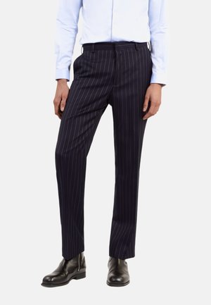 Pantalones de vestir azul oscuro con finas rayas verticales blancas, corte ajustado, frente plano y bolsillos laterales, combinados con botas de cuero negras hasta el tobillo.