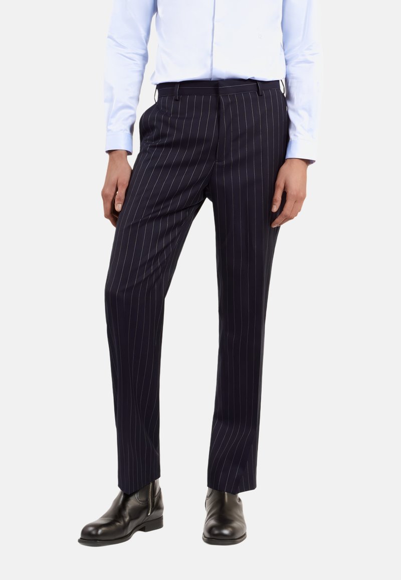 Dunkelblaue Anzughosen mit dünnen vertikalen weißen Streifen, taillierte Passform, flacher Bund und seitlichen Taschen, kombiniert mit schwarzen Leder-Ankle-Boots.