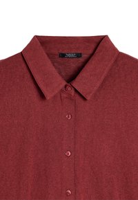 Burgundowa koszulka polo z klasycznym kołnierzykiem, zapięciem na guziki i miękką teksturą. Metka nosi napis "DARTFOIS" w prostym wzorze.