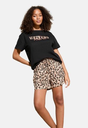 Melna kokvilnas t-kreklā ar uzrakstu "WEEKEND Mode on" treknajā grafikā. Apvienots ar bēšām leopardu raksta šortiem, ar aukliņu jostasvietā.