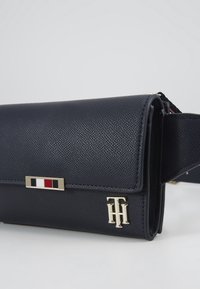 Námořnická texturovaná kožená kabelka s klopovým uzávěrem, zlatými kovovými doplňky a akcentem loga. Obsahuje barevně pruhovaný detail na přední straně.