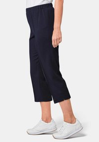 Marineblauwe cropped broek met een elastische tailleband, voorzien van zijsplitten aan de zoom en een zachte textuur, gecombineerd met witte sneakers.