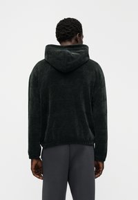 Φούτερ με κουκούλα σε σκούρο πράσινο, από απαλό ύφασμα με διακριτικό ανάγλυφο μοτίβο. Διαθέτει άνετη εφαρμογή και ριμπ τελείωμα, συνδυασμένο με παντελόνι σε σκούρο γκρι χρώμα.