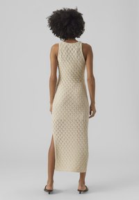 Knitted beige dress with a diamond texture, sleeveless design, and side slit, reaching mid-calf length. Simple and form-fitting silhouette.