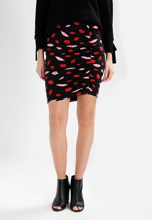 Mini-jupe noire froncée avec imprimés de lèvres rouges et roses, portée avec des bottines noires ouvertes aux orteils et un haut noir à manches longues.