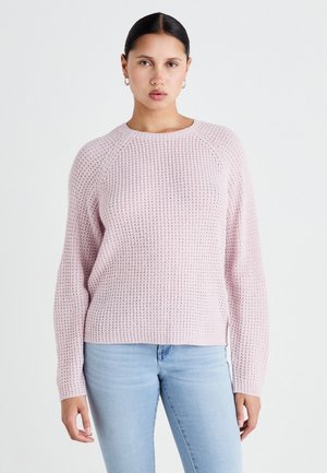Pull en tricot rose clair avec un motif texturé, col rond et manches raglan longues, associé à un jean bleu clair.