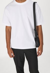 Vit bomullströja med rund halsringning och korta ärmar, i kombination med svarta byxor och en liten svart axelremsväska.