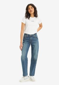 White short-sleeve t-shirt with blue logo, paired with blue straight-leg jeans and white sneakers with blue accents.