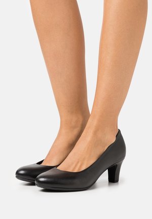 Zapatos de tacón de cuero negro con punta redonda y tacón medio. El diseño presenta una textura suave y un escote bajo.