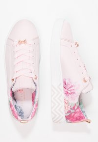 Baskets roses avec des accents floraux, tige en textile lisse, semelle blanche et accessoires en or rose. Comprennent un détail de nœud sur les lacets.