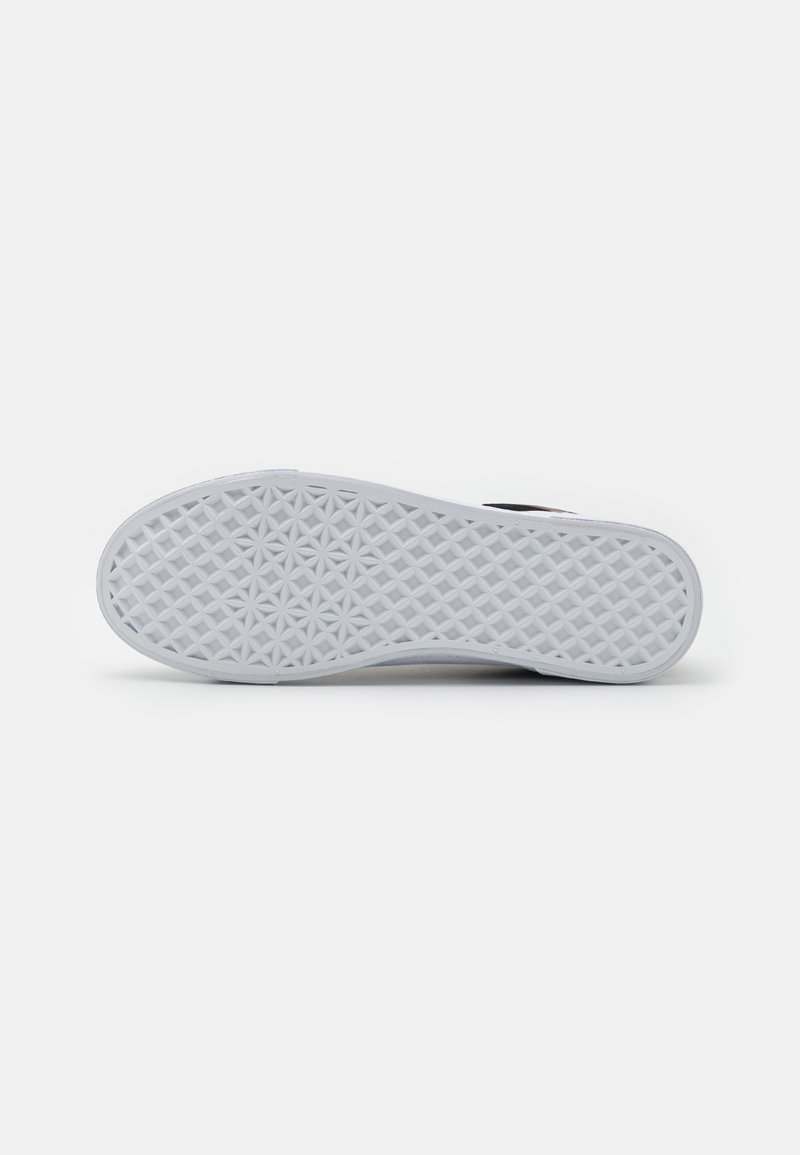 La semelle extérieure de la sneaker blanche présente un motif texturé avec un design géométrique. La semelle est plate et lisse, avec une finition semblable à du caoutchouc.