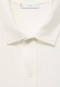 Hvid tekstureret polo skjorte med klassisk krave, knaplukning og subtile stofdetaljer. Etiketten inkluderer mærkenavnet "MNG."