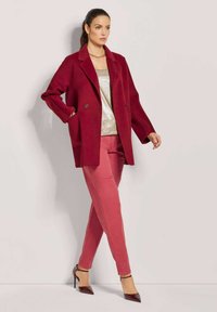 Bordeaux dubbelbreasted jas over een gouden top en roze broek. Kenmerken zijn een gladde stof, een getailleerde snit en hoge hakken.