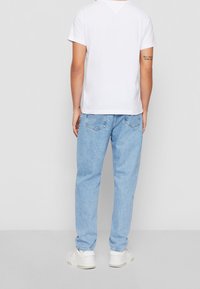 Bílý bavlněný tričko, modré džíny, zobrazeno ze zadní strany. Světlé džíny s pěti kapsami a bílé tenisky. Hladké materiály, volný střih.