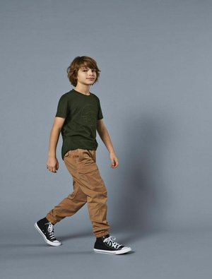 Zielona bawełniana koszulka z logo, beżowe spodnie cargo i czarne sneakersy wysokie z białymi podeszwami. Model spaceruje na szarym tle.