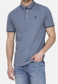 Lichtblauw polo shirt met een kraag, voorzien van zwarte accenten op de mouwen en de kraag, en drie knopen. Gdraag met lichte spijkerbroek.