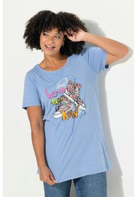 Camiseta de manga corta azul claro con un gráfico de zapatillas altas de flores y el texto "sé el AHORA" en colores vibrantes.