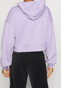 Gekürzter Hoodie in hellem Lavendel, aus weichem Stoff gefertigt. Verfügt über eine Kapuze, übergroße Ärmel und gerippte Bündchen. Kombiniert mit schwarzen Cordhosen.