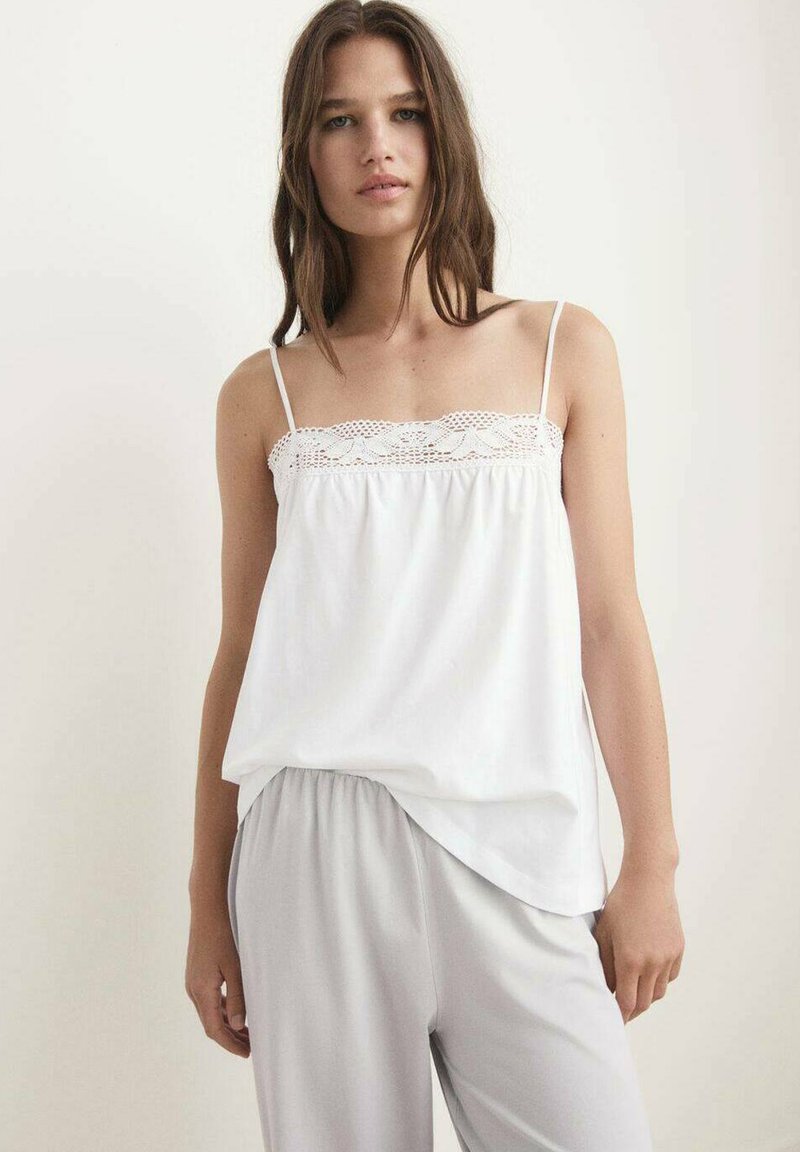 Witte tanktop met kanten rand aan de bovenkant, dunne bandjes en een losse pasvorm, gecombineerd met lichtgrijze broek met elastische taille. Glad textuur van de stof.