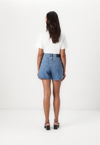Jeanshorts med høy midje, blå farge og en subtil frynsehem. Kombinert med en hvit T-skjorte og svarte hælsandaler.