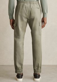 Pantalones cargo de color verde oliva claro con cinturilla elástica, bolsillos laterales y puños elásticos. Tejido suave y ligeramente brillante con un ajuste tailored.