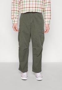 Gröna cargobyxor med avslappnad passform, med sidofickor och en mjuk bomullstextur. Vita sneakers fulländar outfiten.