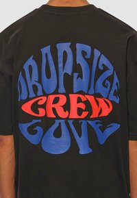 Sort bomulds T-shirt med fed, stiliseret tekst i blå og rød som står "DROPSIZE CREW LOVE" på ryggen, rundede designelementer.