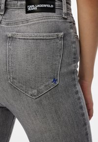 Šedé denimové džínsy s zadnou vreckom so modrým logom 'K' a čiernou etiketou s nápisom "KARL LAGERFELD JEANS." Klasický päť-vreckový dizajn.
