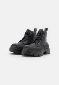 Par de botas de cuero negras de plataforma gruesa con cordones y lengüetas de marca sobre un fondo blanco.