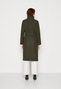 Olive green wool coat with a high collar, belted waist, and long sleeves, extending to knee length. Textured fabric with a smooth finish.