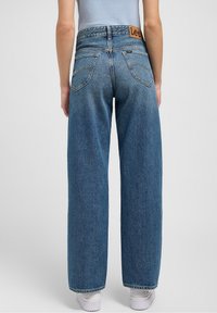 Blue denim high-waisted wide-leg jeans with a leather label on the back and two rear pockets, featuring a slightly faded texture.