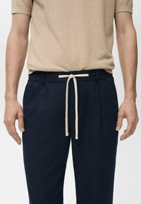 Marineblauwe broek met een elastische tailleband en een beige trekkoord. De stof lijkt zacht en heeft een gladde textuur. De pasvorm is relaxed en casual.