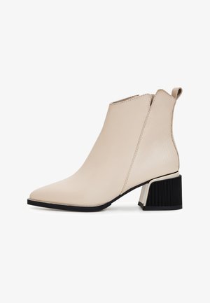Botín beige hasta el tobillo hecho de cuero suave con punta afilada, detalles acanalados en la parte posterior y un tacón negro en bloque.