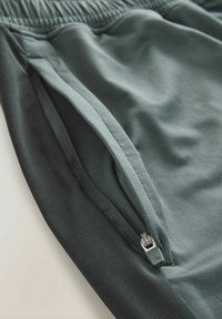Sorte atletiske shorts med en lys grå lynlåslomme, der har en struktureret talje og glat stof. Stof har en let glans og stræk.