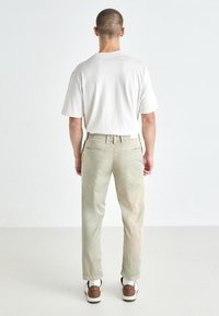 Lys beige bomullsbukser med en avslappet passform, med baklommer og subtile teksturerte detaljer. Kombinert med en løs hvit skjorte og sneakers.
