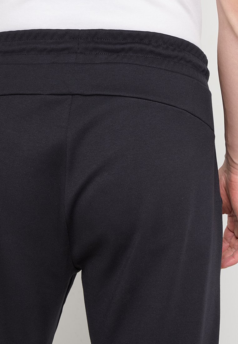 Pantaloni sportivi neri con un tessuto morbido e elasticizzato, dotati di una vita elasticizzata, che mostrano una texture liscia e un design aderente.