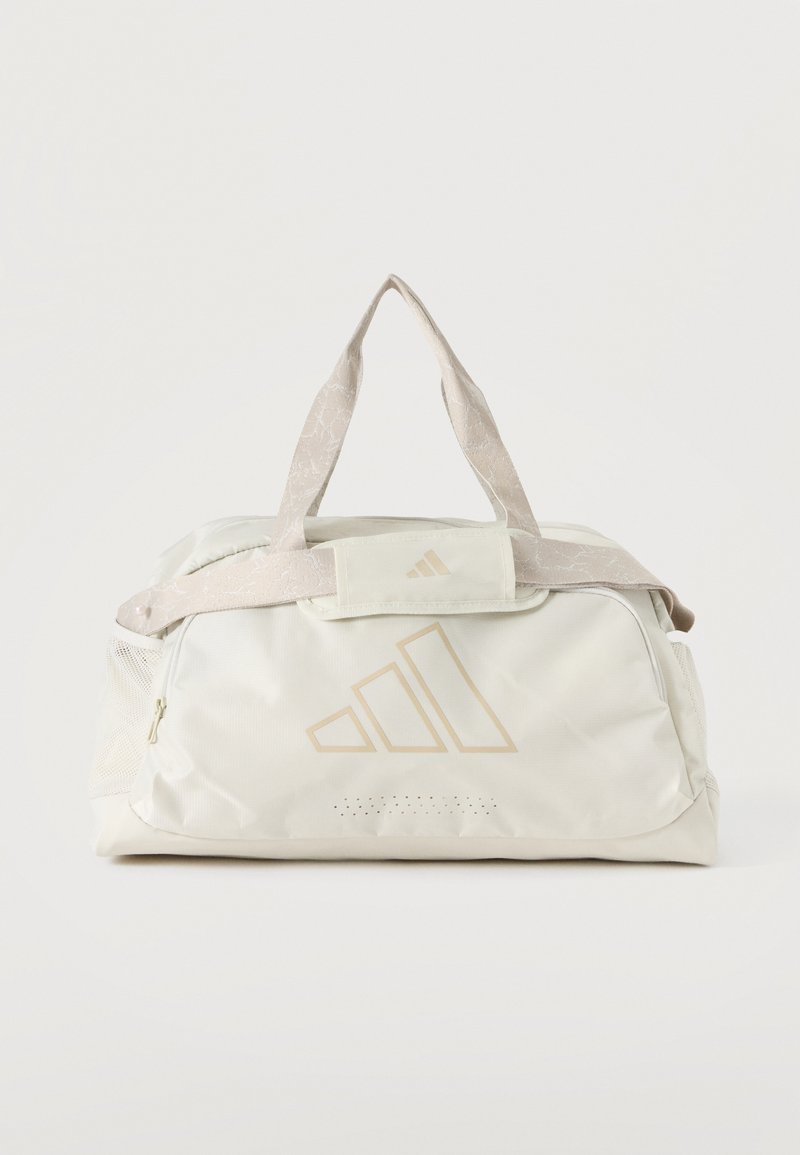 Sac de sport blanc avec des accents beiges, doubles poignées, poches latérales en maille et un logo discret à l'avant.