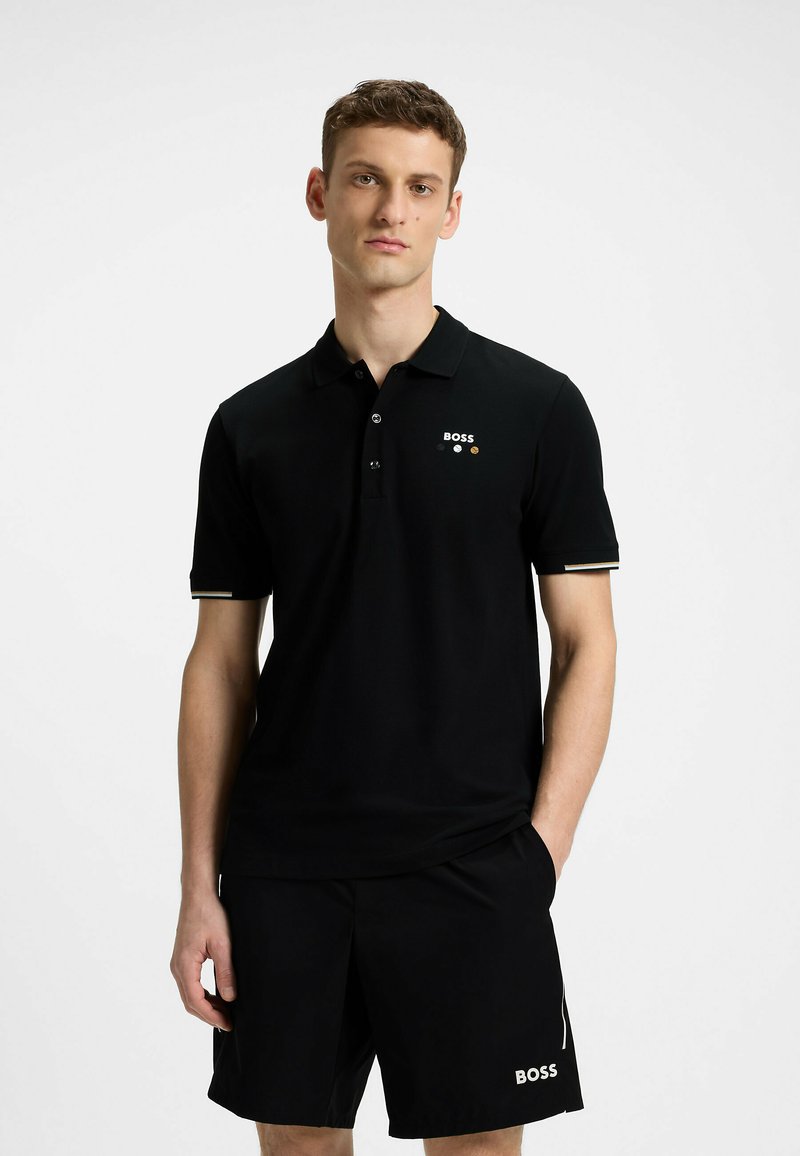 Czarna koszulka polo z krótkimi rękawami, trzema guzikami i logo marki w białych i złotych akcentach. Noszona z czarnymi szortami z logo.