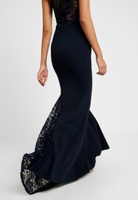 Granatowa sukienka o dopasowanej sylwetce, z koronkowym panelem u dołu i rozkloszowanym dolnym częścią. Gładki materiał i misternie zdobiona koronka.