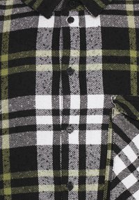 Camicia a quadri nera, bianca e verde oliva con design a bottoni, colletto e taschino sul petto. Realizzata in tessuto testurizzato.